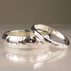 two silver wedding rings sitting next to each other on a white surface with reflections in the background