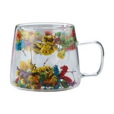 a glass mug filled with colorful flowers on top of a white surface