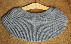 a gray knitted bib with wooden hanger on the top, sitting on a carpeted floor