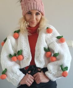 a woman wearing a knitted jacket with carrots on it and a pink hat