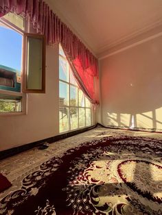 an empty room with red curtains and rugs in front of large windows overlooking the city