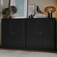 a black cabinet sitting on top of a wooden floor next to a lamp and pictures