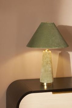 a green lamp sitting on top of a wooden table next to a white dresser with drawers