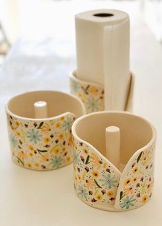 three flowered cups are sitting on a table next to a roll of toilet paper