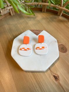 an orange and white pair of earrings sitting on top of a wooden table next to a potted plant