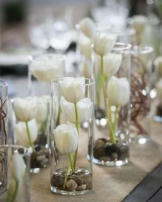 there are many vases with white flowers in them on the table cloth, along with rocks and pebbles