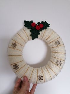 a hand is holding a knitted christmas wreath with holly leaves and red berries on it