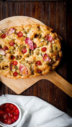 a pizza sitting on top of a wooden cutting board next to a bowl of tomatoes