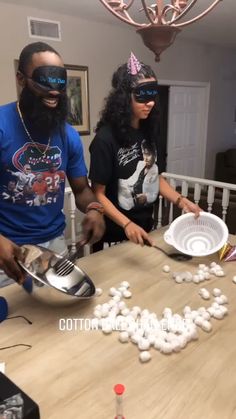 two people standing around a table with plates and bowls on it, one person wearing blindfolds