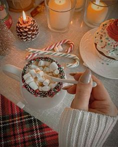 a person holding a cup filled with marshmallows next to a christmas cake