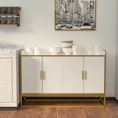 a white and gold sideboard with cups on it in front of a framed photograph