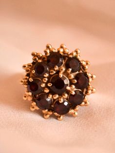 This big, bold, statement ring will enter the room before you do; fashioned in nicely toned 14kt yellow gold, it is crafted with a large, circular setting embellished with stunning beaded trios all around the circumference, creating a very bohemian granulated aesthetic. It is stunningly set with 9 glittering garnet stones, deeply wine coloured, catching the sunlight so strikingly. The garnets all bear moderate to heavy inclusions, lending them such a moody, mysterious presence that will mesmeriz Garnet Stone, Wine Colored, Vintage Bohemian, Cluster Ring, Statement Ring, Unique Rings, Prong Setting, Beautiful Rings, Favorite Jewelry