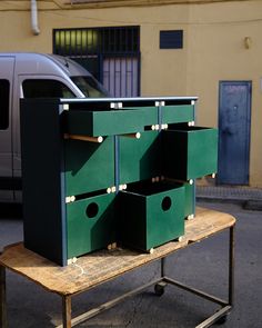 a table with four green boxes on it in front of a building and a car