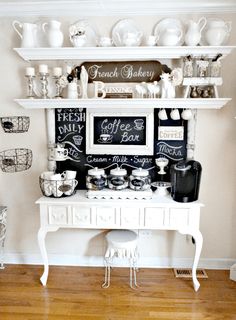 a white table topped with lots of cups and saucers next to a wall mounted chalkboard