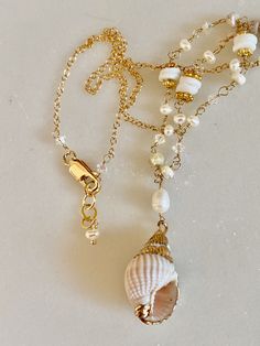 The perfect necklace for a beach vacation or wedding! A gold tipped shell hangs from chain made from pukka shells, pearls, and white crystals as well as gold filled chain and clasp. Each piece is individually wire wrapped to create this unique necklace.  In their native Hawaii, pukka shells traditionally bestow good luck.  Pearls are the ultimate symbol of wisdom. They are also associated with purity and innocence. Valued for their calming effect, pearls represent serenity and are also the birth White Shell-shaped Pearl Drop Necklace, Beach Shell Necklace With Pearl Charm, Shell Necklace With Pearl Charm For Beach, Shell-shaped Necklace With Pearl Charm For Beach, Shell Shaped Necklace With Pearl Charm For Beach, Elegant Necklace With Lobster Clasp For Vacation, Vacation Pearl Charm Shell Necklace, Beach Shell Shaped Pearl Pendant Jewelry, Vacation Shell Necklace With Pearl Charm