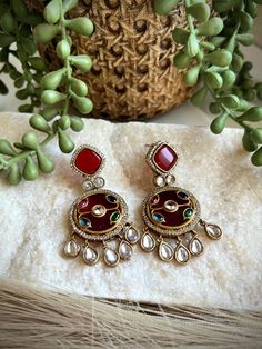 These exquisite earrings are handcrafted with intricate inlay work, featuring vibrant semi-precious stones set in a rich, red background. The intricate design is adorned with glistening crystals and accented with delicate crystal drops, creating a stunning and eye-catching pair of earrings. Crafted with meticulous attention to detail, these earrings are a true work of art. The inlay technique showcases the skill and artistry of the craftsperson, resulting in a unique and timeless piece of jewelry. Whether for a special occasion or as an everyday accessory, these earrings are sure to elevate any outfit and add a touch of elegance. Perfect for those who appreciate exquisite craftsmanship and one-of-a-kind designs. ------------------------------------------------------------------------------ Multicolor Fusion Style Gemstone Earrings, Elegant Jeweled Earrings For Diwali, Fusion Style Chandelier Earrings As Gift, Jeweled Round Metal Earrings, Jeweled Drop Earrings For Festivals, Traditional Jeweled Dangle Danglers, Jeweled Drop Danglers For Festivals, Elegant Multicolor Ruby Jewelry, Multicolor Stone-set Jewelry For Celebrations