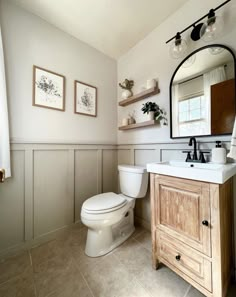 a white toilet sitting next to a wooden cabinet in a bathroom under a large mirror