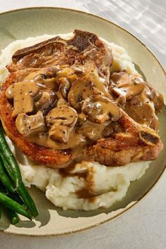 a plate with mashed potatoes, green beans and meat covered in mushroom gravy