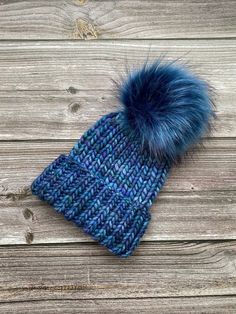 a blue knitted hat with a fur pom - pom sitting on top of it