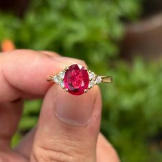 a person holding a ring with a large red stone in it's middle finger