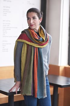 a woman standing in front of a table wearing a multicolored knitted scarf