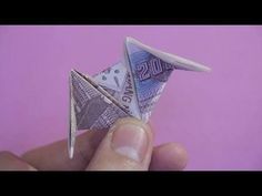 a hand holding a small origami bird made out of money on a purple background