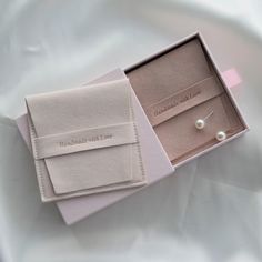 two pairs of earrings in a box on a white sheet with a pink ribbon around it