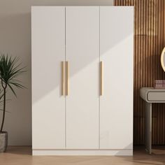 a white cabinet with gold handles next to a potted plant and mirror on the wall