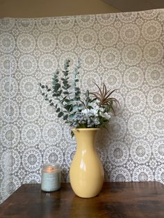 a yellow vase filled with flowers sitting on top of a wooden table next to a candle