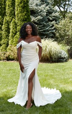 a woman in a white dress is posing for a photo on the grass with trees behind her