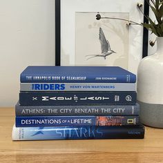 a stack of books sitting on top of a wooden table next to a white vase