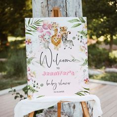 a welcome sign for a baby shower with animals and flowers on it, in front of a tree