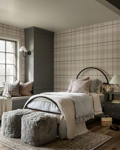 a bedroom with plaid wallpaper and bedding in the corner, along with two ottomans