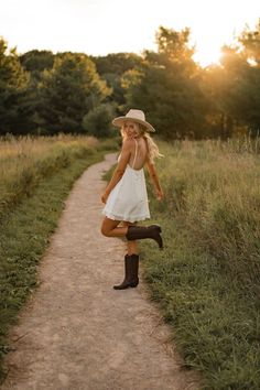 a woman in white dress and cowboy hat standing on dirt path