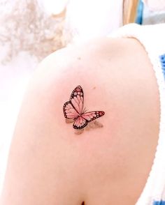 a small pink butterfly tattoo on the back of a woman's upper arm and shoulder