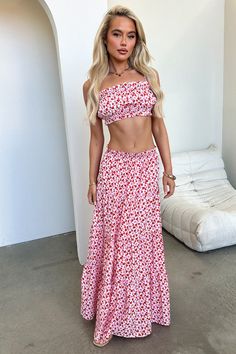 a woman in a red and white floral print two piece dress standing next to a bed