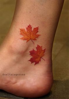 a leaf tattoo on the foot of a woman's feet with red and orange leaves