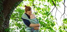 a woman holding a baby in her arms while standing next to a tree with green leaves