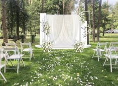 an outdoor ceremony setup with white chairs and flower petals on the grass, surrounded by trees