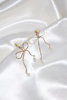 gold bow stud earrings pearl dangling fashion accessory jewelry stainless steel hypoallergenic water resistant tarnish free Elegant Wire Wrapped Earrings For Formal Occasions, Trendy Dangle Pearl Drop Earrings, Trendy Pearl Drop Dangle Earrings, Wire Wrapped Metal Earrings For Party, Trendy Pearl Charm Drop Earrings, Party Wire Wrapped Metal Earrings, Elegant Wire Wrapped Drop Linear Earrings, Elegant Metal Single Wrap Earring, Elegant Single Metal Wrap Earring