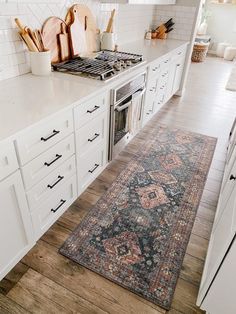 a kitchen with white cabinets and an area rug in front of the stove top oven