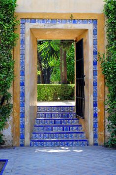 an entrance to a building with blue and white tiles on the walls, surrounded by greenery