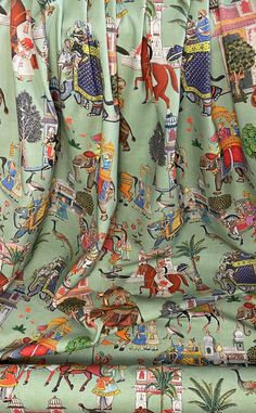 the back of a couch covered in a green fabric with colorful images on it and people riding horses