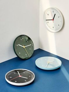 two clocks sitting next to each other on top of a blue table with white walls