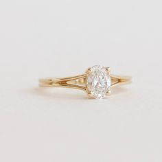 a yellow gold engagement ring with an oval cut diamond in the center, on a white background