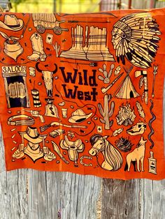 an orange towel with wild west images on it hanging from a wooden fence in front of a building