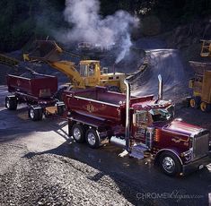 two dump trucks parked next to each other on a gravel road with machinery in the background