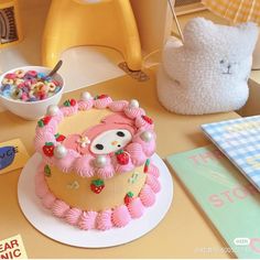 a hello kitty themed cake on a table next to a teddy bear and bowl of cereal