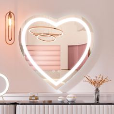 a heart shaped mirror hanging on the side of a wall next to a vase with flowers