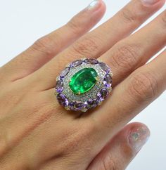 This stunning ring features a large oval-shaped diamond-cut emerald nestled atop a bouquet of beautifully assorted oval amethyst gemstones, accented by a melee of sparkling white sapphires. The intricate design is set on a 14K yellow gold plated sterling silver band, creating a luxurious and elegant piece. Technical Specifications  -Gemstones: Emerald, Amethyst, White Sapphire -Metal: Sterling 925 Silver -Plating: 14K Yellow Gold -Net Metal Weight: 5.292 grams -Gross Weight: 7.8 grams -Gemstone Luxury White Gold Jewelry With Green Amethyst, Luxury Oval Emerald Cluster Ring, Green Multi-stone Oval Diamond Ring, Oval Green Multi-stone Diamond Ring, Green Oval Multi-stone Diamond Ring, Exquisite Oval Emerald Ring, Luxury Green Oval Cluster Ring, Oval Multi-stone Emerald Ring, Green Oval Cluster Ring Fine Jewelry